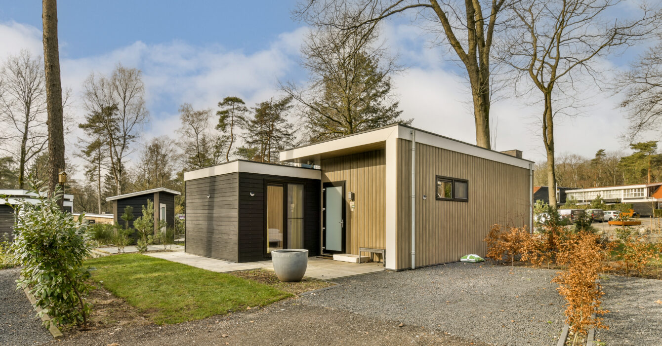 a small wooden house with a gravel driveway and trees